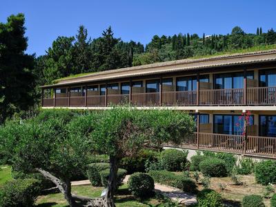 Modern hotelgebouw met twee verdiepingen en balkons, omgeven door bomen en struiken.