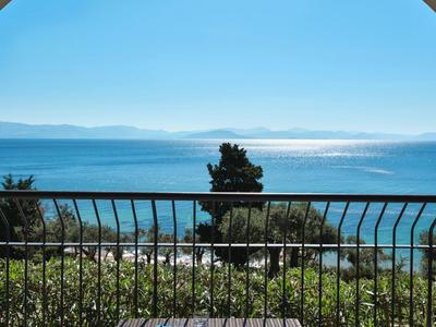 Balkon mit zwei Stühlen, Tisch, Blick auf Meer, grünes Gestrüpp und blauem Himmel im Hintergrund.