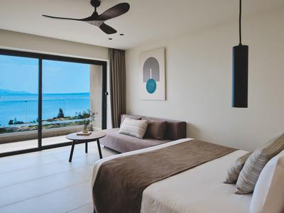 Moderne hotelkamer met bed, bank en zeezicht door grote ramen.