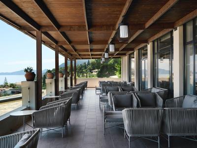 Overdekt hotelterras met fauteuils en tafels met uitzicht op water en bergen.