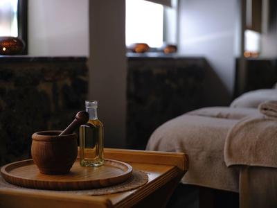 Ein Holztisch mit einer Runde Platte, einem Mörser und einem Fläschchen Öl neben einer Massageliege.