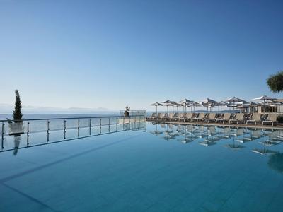 Ein Infinity-Pool mit Blick auf das Meer und Sonnenliegen unter weißen Sonnenschirmen.