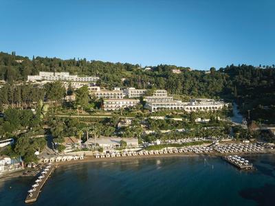 Hotelanlage am Hang mit Pool, Strandliegen und Blick auf das blaue Meer unter klarem Himmel.