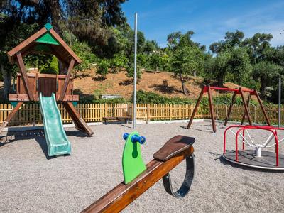 Kinderspielplatz mit Rutsche, Schaukel und Karussell in einer sonnigen Gartenanlage.