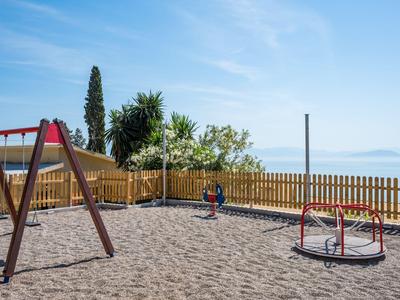 Spielplatz am Strand mit Sandboden, Schaukeln und Meerblick im Hintergrund.