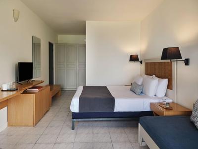 Modernes Hotelzimmer mit Doppelbett, TV, Sideboard und kleinem Sofa in neutralen Tönen.