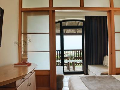 Wohnzimmer mit Sofa, Holzregal und Blick auf Balkon mit Meerblick.