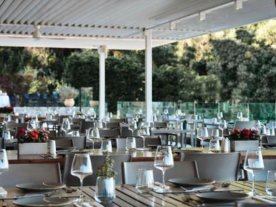 Modernes, überdachtes Hotelrestaurant mit weißen Tischen, Stühlen und Weingläsern im Freien.