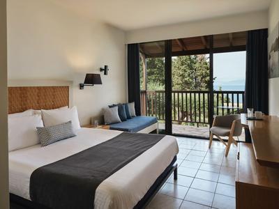 Modern eingerichtetes Hotelzimmer mit Doppelbett, Sofa und Blick auf einen Balkon mit Naturkulisse.