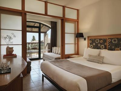 Helles Hotelzimmer mit Doppelbett, Holzmöbeln und Terrasse mit Blick auf Bäume.