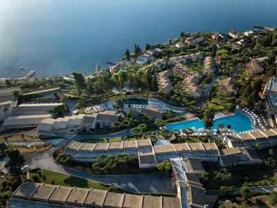 Blick auf ein Resort mit Pool und Blick aufs Meer, umgeben von grünen Hügeln.