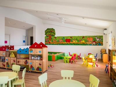 Helles, farbenfrohes Kinderspielzimmer mit Tischen, Stühlen und Regalen in einem Hotel.