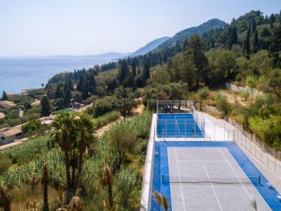 Uitzicht op tennisbaan en zwembad met zee en heuvels op de achtergrond