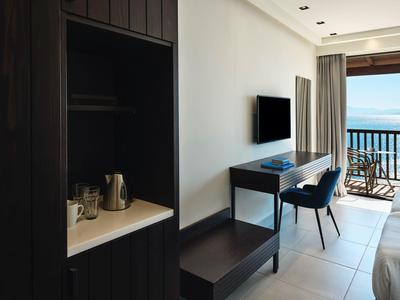 Moderner Hotelraum mit Schreibtisch, Fernseher, Stuhl, Teekocher und Balkon mit Meerblick.