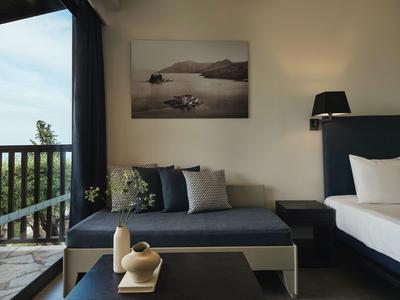 Moderner Hotelraum mit blauem Sofa, Kissen, schwarzem Nachttisch und Balkon mit Aussicht.