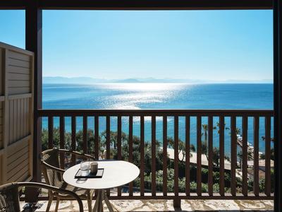 Balkon mit rundem Tisch und Stuhl, Blick auf Meer und bewaldete Küste bei klarem Himmel.