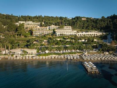 Strand mit Liegestühlen und Palmen vor großen terrassenförmigen Hotelgebäuden unter blauem Himmel.