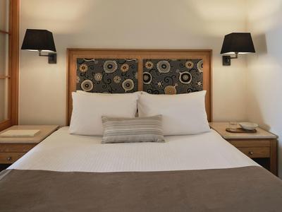 Doppelbett mit weißen Kissen, brauner Decke, gemustertem Kopfteil und schwarzen Wandlampen.