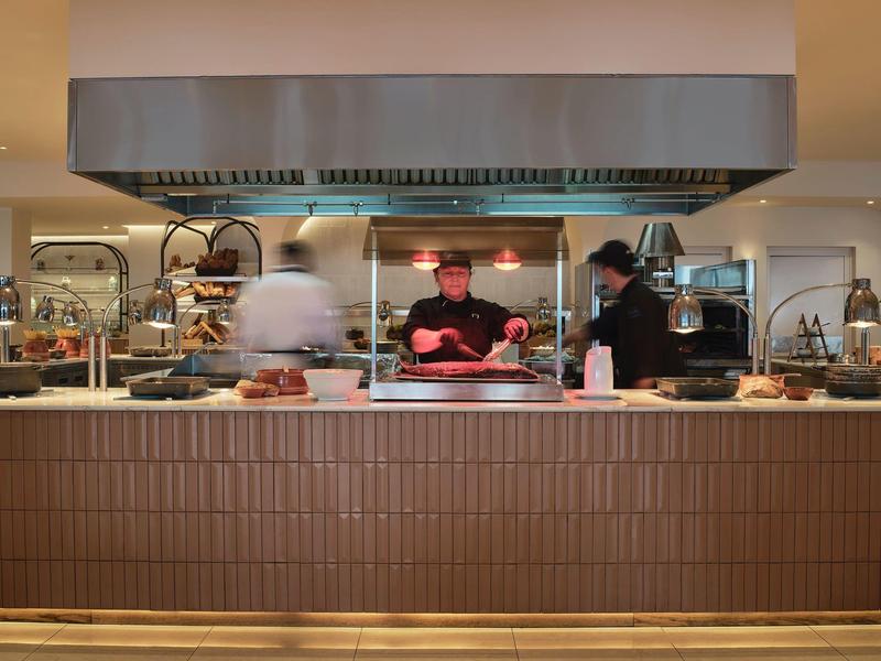 Küchenbereich mit drei Personen, großem Dunstabzug und brauner Kacheltheke in Restaurant.