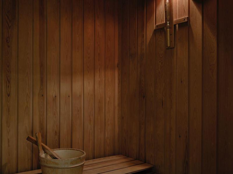 Holzsauna mit Sitzbank, Holzeimer und Schöpfkelle, warme Beleuchtung an der Wand.