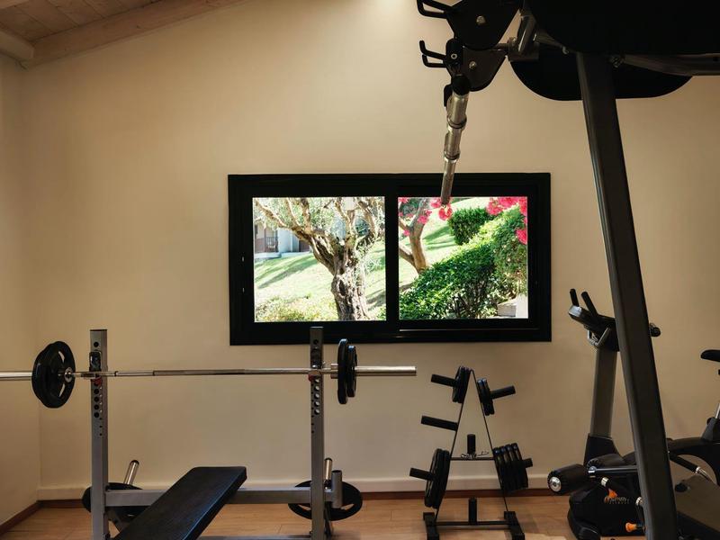 Moderne Heim-Fitness mit Hantelbank, Gewichten, Krafttrainingsgerät und großen Fenstern unter Holzdach.