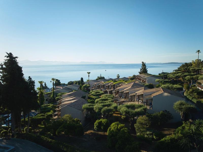 Blick auf Resort-Häuser mit grünen Bäumen und Blau des ruhigen Meeres im Hintergrund.