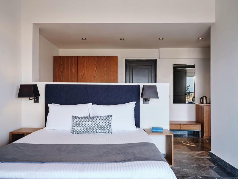 Modernes Schlafzimmer mit großem Bett, dunkelblauem Kopfteil, Holzmöbeln und Wandlampen.