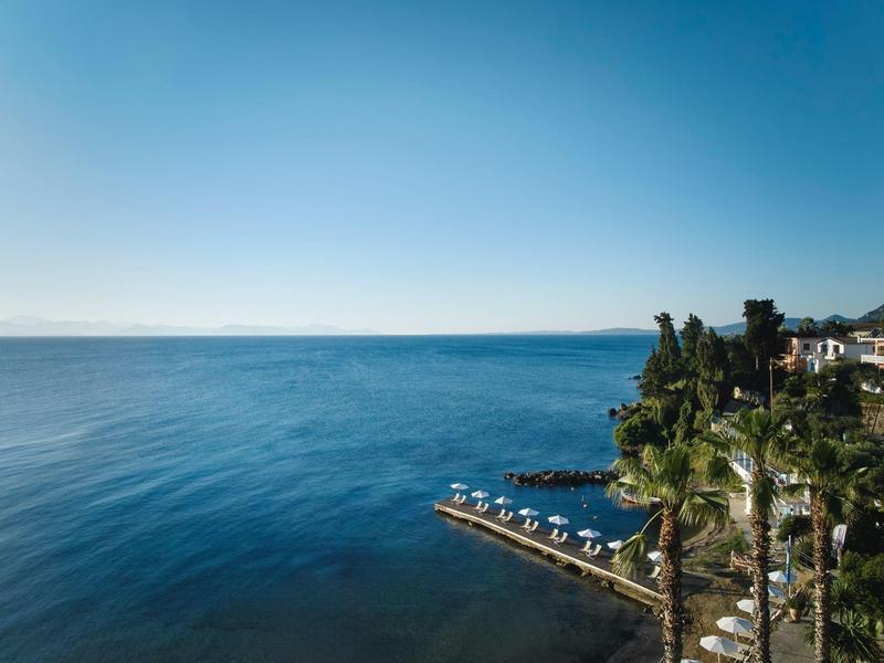 Klares blaues Meer mit Holzstegen und Palmen am Ufer unter hellem Himmel.