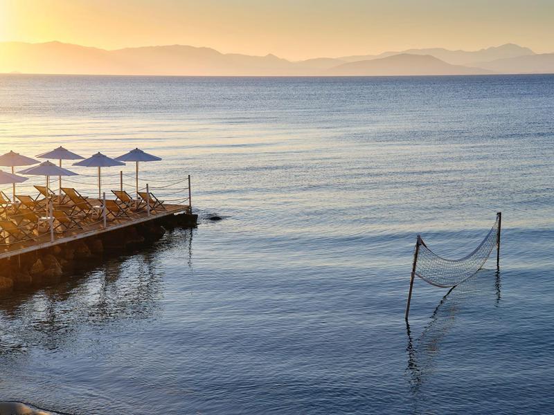 Strand mit Sonnenschirmen neben ruhigem Meer und eingeschwungenem Volleyballnetz bei Sonnenuntergang.