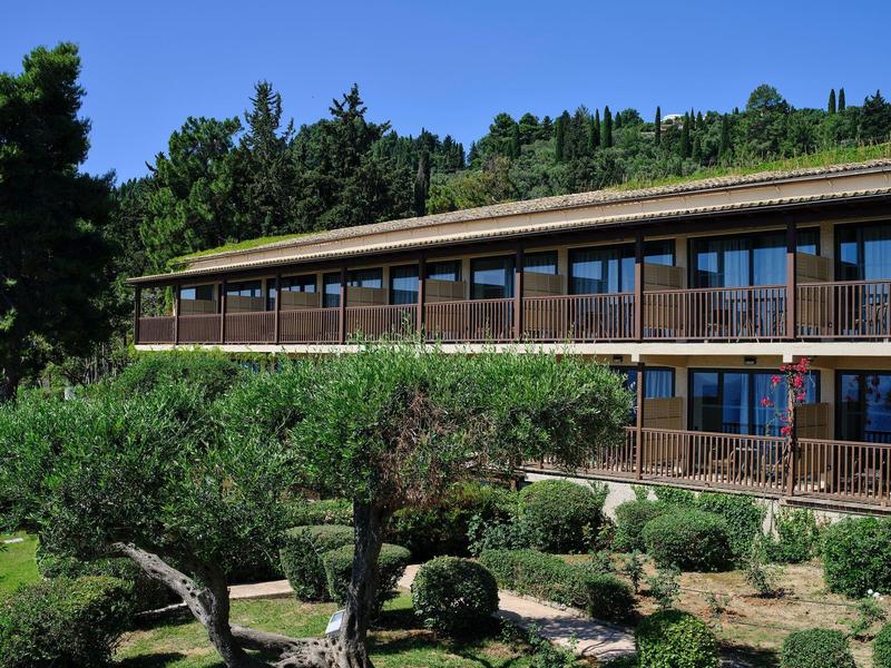 Modernes zweistöckiges Gebäude mit großer Terrasse und grünen Bäumen im Vordergrund.