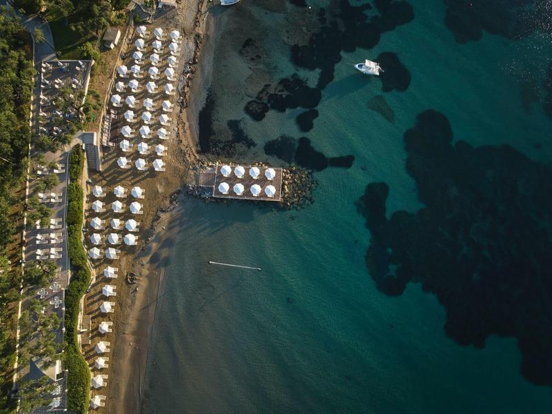 Luftaufnahme einer Küste mit Reihen von weißen Sonnenschirmen und klar blau-grünem Wasser.