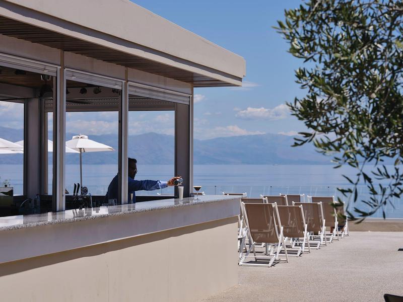 Moderner Außenbereich mit Stühlen, Glasfronten und Blick auf Berge und See im Hintergrund.