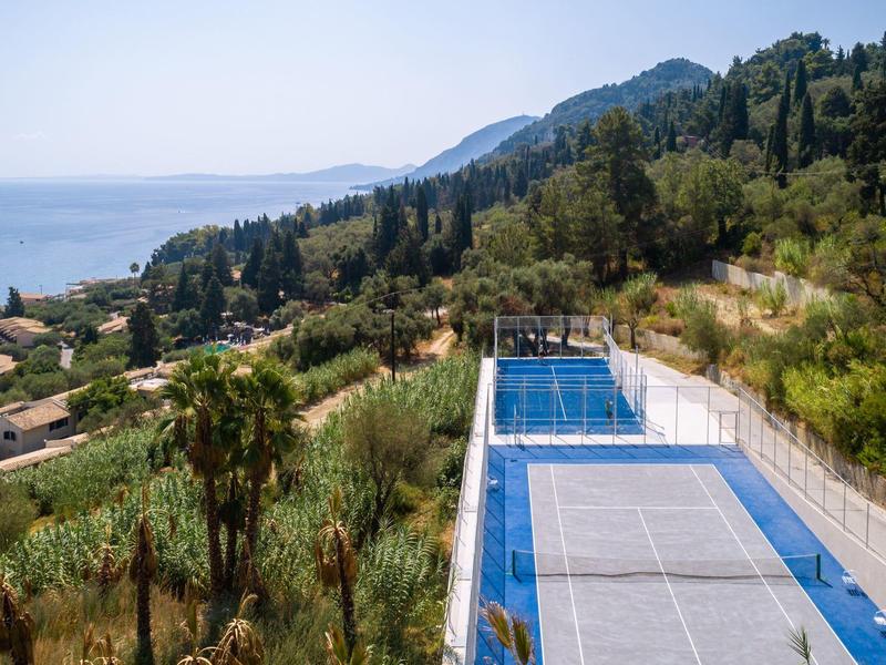 Sportanlage mit Tennisplatz neben Wald und Meerblick an einem sonnigen Tag.