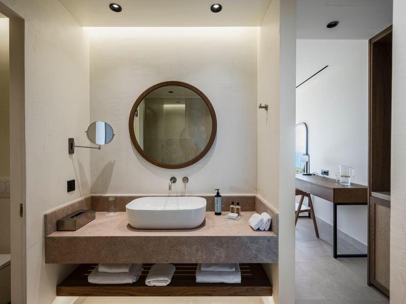 Modernes Badezimmer mit großem rundem Spiegel, weißem Waschbecken und offenem Unterschrank.