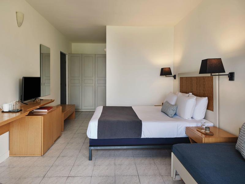 Helles, modernes Schlafzimmer mit Doppelbett, grauen Akzenten, TV und Holzmöbeln.