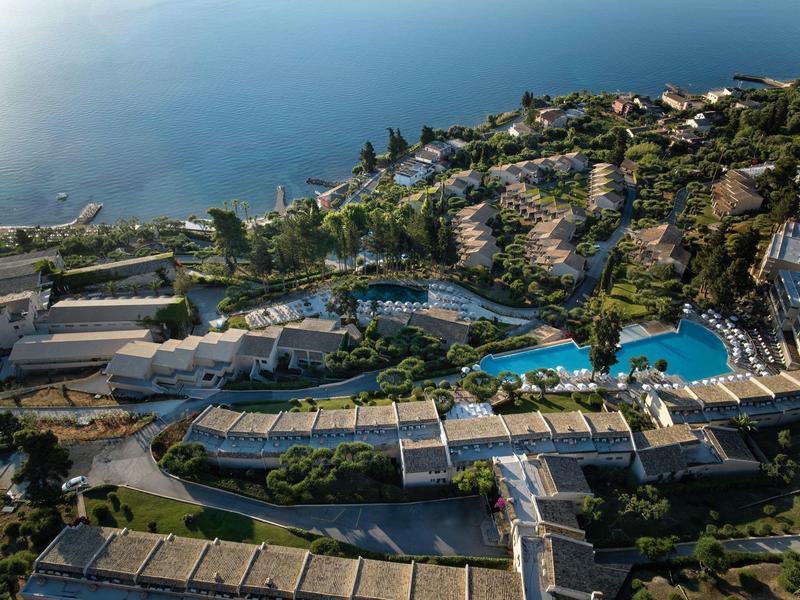 Luftaufnahme eines Resorts mit mehreren Pools, grüner Vegetation und Blick auf das blaue Meer.