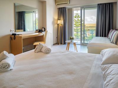 Helles Hotelzimmer mit großem Bett, Couch, Schreibtisch und Balkon mit Meerblick.