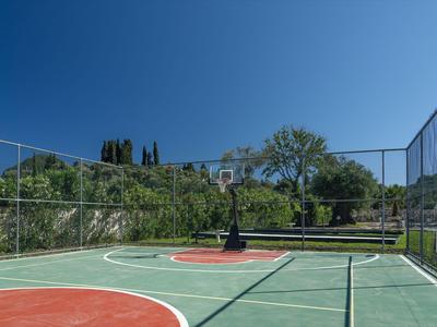 Un terrain de basket-ball extérieur vide entouré d'une clôture et d'arbres sous un ciel clair.