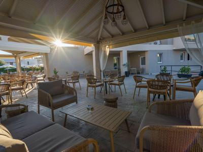 Terrasse couverte confortable avec sièges et tables dans un espace hôtelier au coucher du soleil.