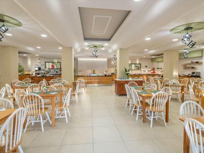 Großer heller Speisesaal mit Holztischen und weißen Stühlen unter Deckenspots.