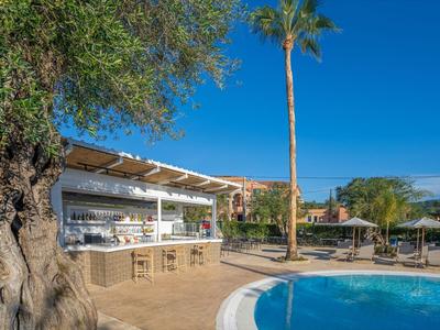 Espace extérieur d'un hôtel avec piscine, bar, tabourets hauts et palmiers sous un ciel dégagé.