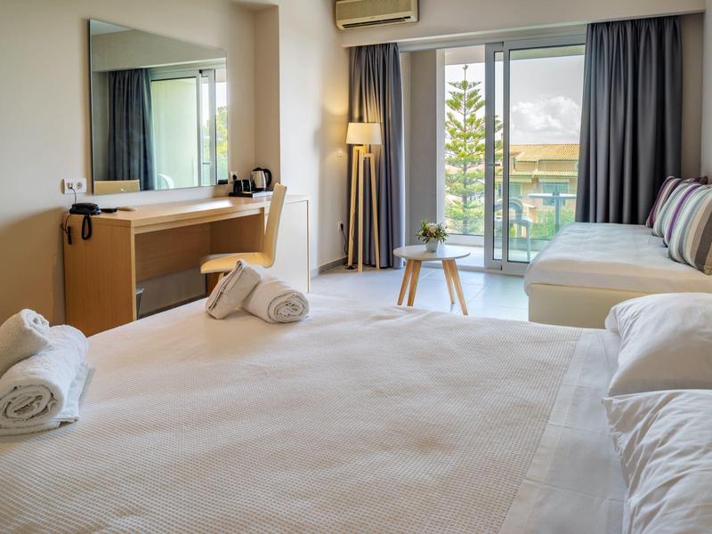 Helles Hotelzimmer mit großem Bett, Couch, Schreibtisch und Balkon mit Meerblick.