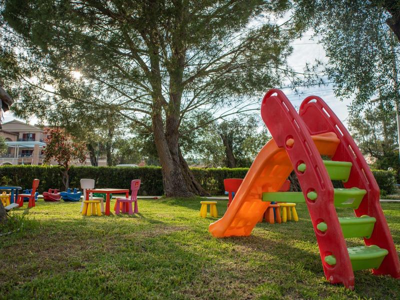 Bunter Kinderspielplatz mit Rutsche, Tischen und Stühlen im grasbewachsenen Park.