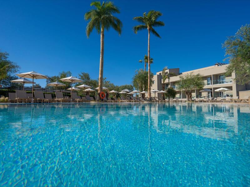 Großer Hotelpool mit Palmen und Sonnenschirmen bei klarem Himmel