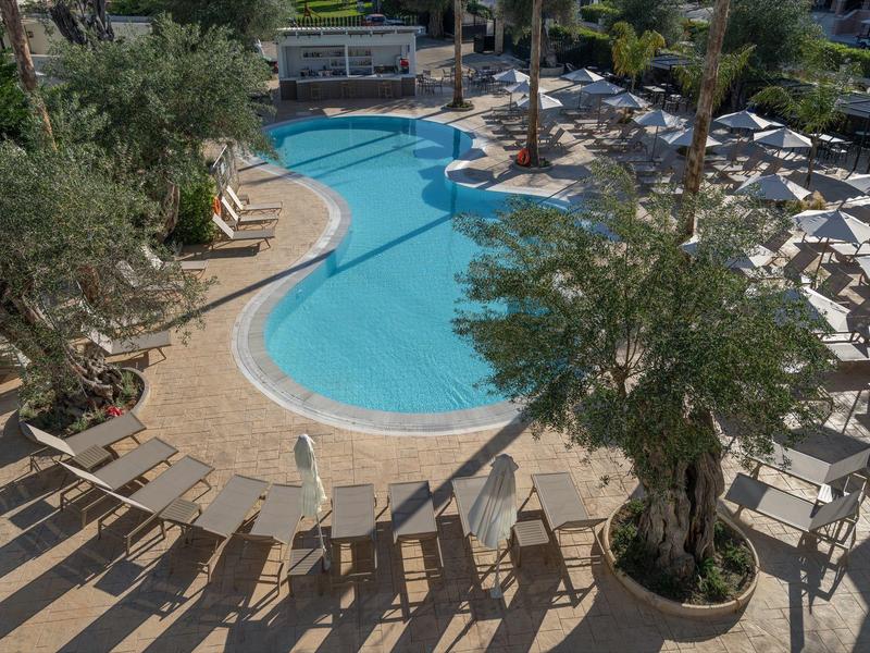 Ein sonniger Außenpool mit Liegestühlen und Sonnenschirmen, umgeben von Bäumen.