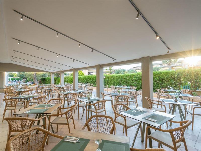 Überdachter Außenbereich eines Restaurants mit Holz- und Flechtstühlen und Tischen.