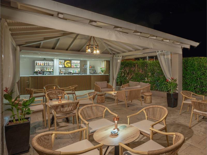 Gemütliche Terrasse mit Korbmöbeln und Barbereich unter Holzpavillon bei Nacht