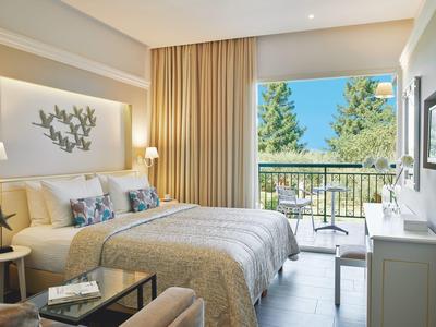 Helles Schlafzimmer mit Doppelbett, grauer Bettdecke, Balkon und Blick auf grüne Bäume.