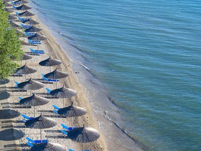Strand mit Reihen von blauen Liegestühlen und Strohmatschirmen entlang des klaren, ruhigen Meeres.
