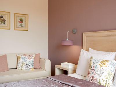 Gemütliches Schlafzimmer mit beigem Sofa, Holzbett, Blumenbildern und pastellfarbenen Kissen.